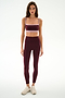 A woman stands against a plain background wearing the SPLITS59 Clare High Waist Rigor 7/8 leggings in Dark Cherry/Blush, paired with a matching burgundy sports bra and white athletic shoes.
