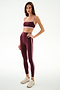 A woman models the SPLITS59 Clare High Waist Rigor 7/8 leggings in Dark Cherry/Blush, paired with a matching sports bra and white sneakers, standing against a plain white background.