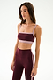 A woman stands against a plain white background wearing the SPLITS59 Monah Rigor Bra in Dark Cherry/Blush with matching high-waisted leggings featuring light pink trim.