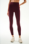 A person is wearing SPLITS59 Clare High Waist Rigor 7/8 leggings in Dark Cherry/Blush, featuring a sculpting high-waisted fit, paired with white sneakers and standing against a plain light background.