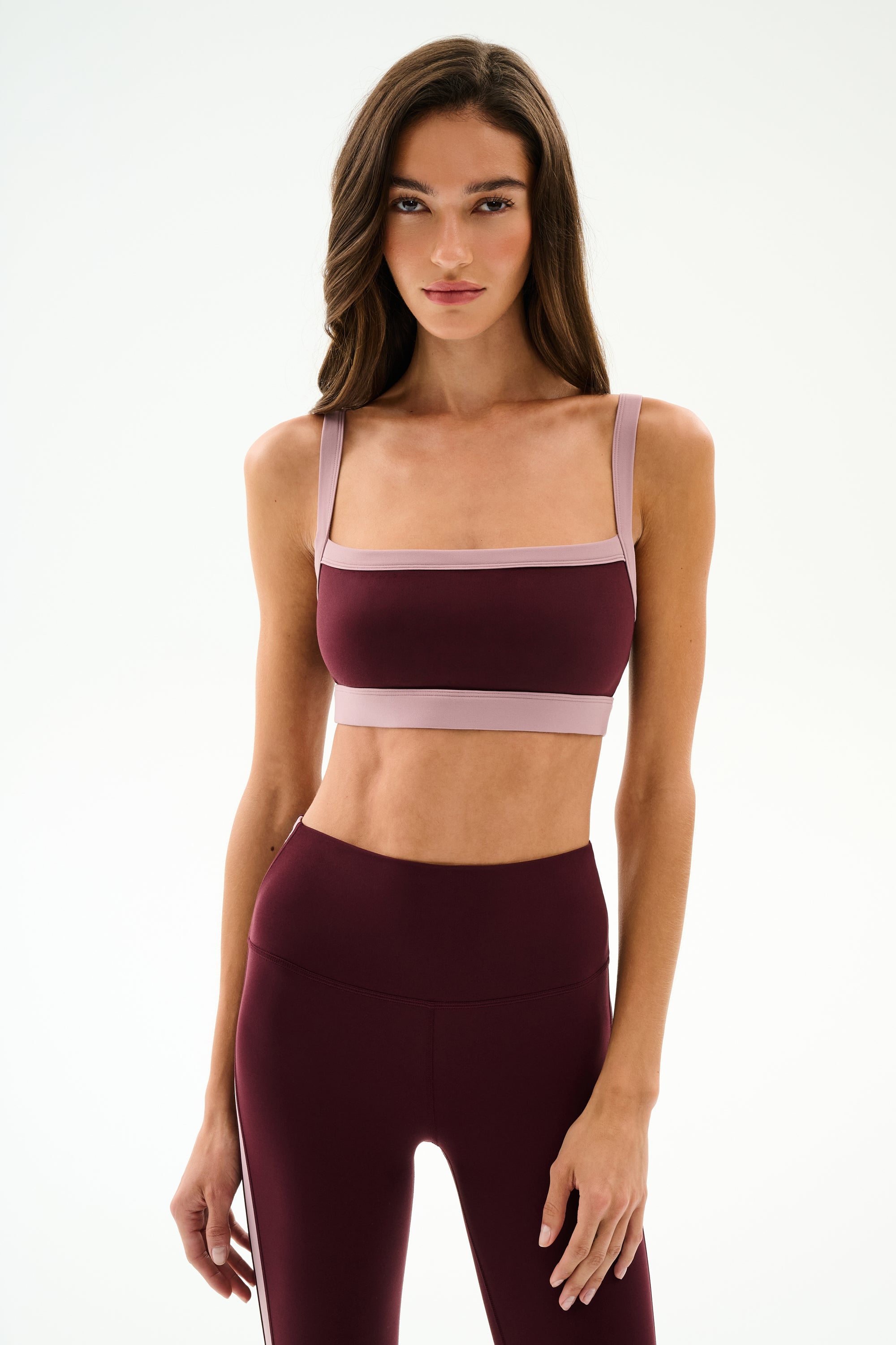 A woman wearing the SPLITS59 Monah Rigor Bra in Dark Cherry/Blush with coordinating high-waisted leggings, standing against a plain white background.