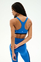 A woman models the SPLITS59 Maci Airweight Bra in Classic Blue/Indigo, paired with matching leggings made from a smooth nylon-spandex blend. She stands with her back to the camera, her left hand holding her right wrist against a plain white background.
