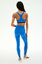 A person stands facing away wearing the SPLITS59 Ella High Waist Airweight 7/8 leggings in Classic Blue/Indigo with a matching sports bra and white athletic shoes, set against a plain light background.