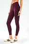 A person wears SPLITS59's Mia Rigor Legging w/ Stripe in Dark Cherry/Indigo, paired with cream sneakers featuring maroon stripes, standing against a plain white background.