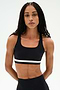 A woman with long braided hair wears the SPLITS59 Miles Rigor Bra in Black/White, paired with matching leggings, standing against a plain white background with her hands behind her back.