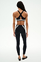 A person faces away, wearing SPLITS59’s Miles High Waist Rigor 7/8 leggings in Black/White with a black crisscross sports bra, set against a plain white background.