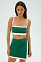 The woman exudes effortless style in the SPLITS59 Monah Rigor Bra - Arugula/White, paired with a matching skirt, as she strikes a yoga-inspired pose against a serene light background.