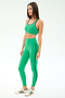 A woman wears SPLITS59’s Amber Airweight High Waist 7/8 leggings in Spearmint/Military with matching sports bra and white sneakers with green accents, standing against a plain light background.