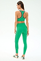 A woman faces away in the SPLITS59 Robbie Airweight Bra - Spearmint/Military, paired with matching leggings and white sneakers, against a plain light background.
