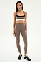 A woman poses against a plain background in SPLITS59's Layla Airweight High Waist 7/8 leggings in Lentil/Black—breathable and perfect for hot yoga.