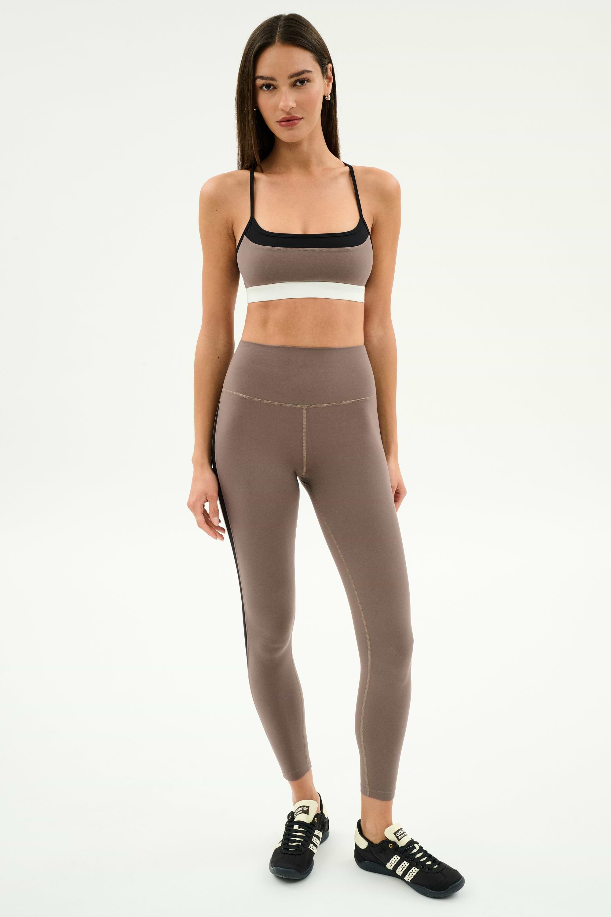A woman poses against a plain background in SPLITS59's Layla Airweight High Waist 7/8 leggings in Lentil/Black—breathable and perfect for hot yoga.