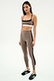 A woman stands against a white background wearing SPLITS59 Layla Airweight High Waist 7/8 leggings in Lentil/Black stripes, paired with a beige sports bra and black athletic shoes—ideal for hot yoga or any workout.