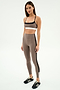 A woman in a neutral pose wears the SPLITS59 Scottie Airweight Bra in Lentil/Black, paired with high-waisted leggings and black athletic shoes, standing against a plain white background.