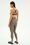 A woman stands facing away, wearing the SPLITS59 Layla Airweight High Waist 7/8 leggings in Lentil/Black, featuring black crisscross straps and ultra-light Airweight fabric—ideal for hot yoga—paired with black athletic shoes.