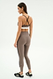 A woman stands facing away, wearing the SPLITS59 Layla Airweight High Waist 7/8 leggings in Lentil/Black, featuring black crisscross straps and ultra-light Airweight fabric—ideal for hot yoga—paired with black athletic shoes.