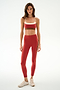 Woman wearing SPLITS59 Scottie Airweight Bra - Terracotta/Creme and matching high-waisted leggings with side stripes, paired with beige sneakers on a white background.