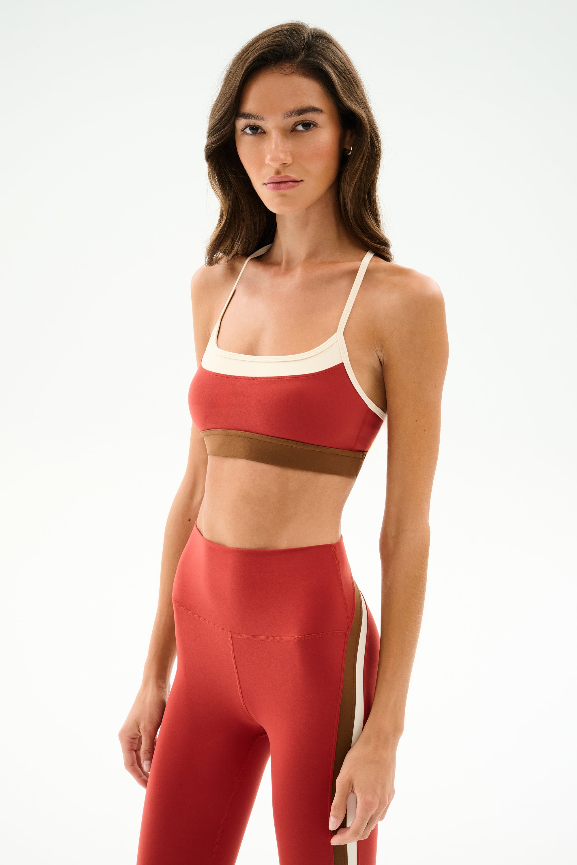 Woman wearing the SPLITS59 Scottie Airweight Bra - Terracotta/Creme with matching high-waisted leggings, standing against a plain white background.