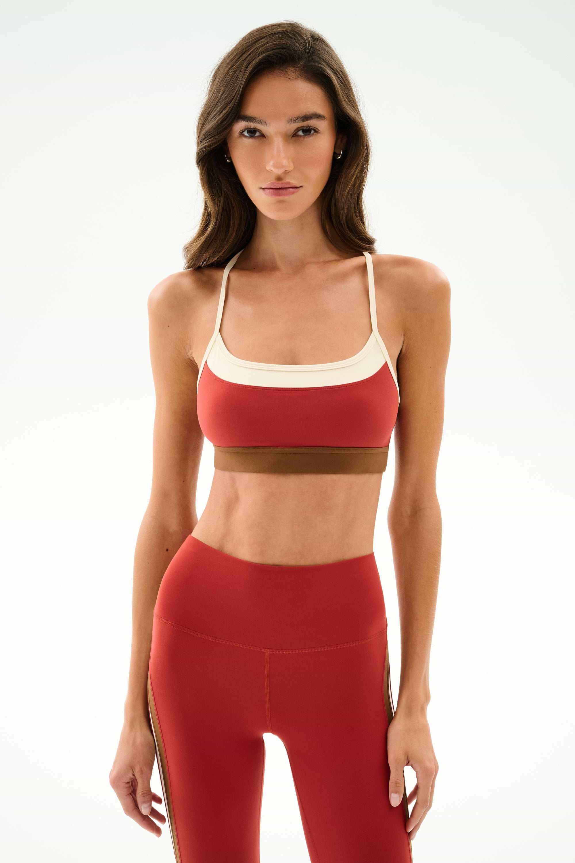 Woman standing facing forward, wearing the SPLITS59 Scottie Airweight Bra - Terracotta/Creme with matching high-waisted leggings, against a plain light background.