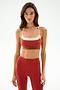 Woman standing facing forward, wearing the SPLITS59 Scottie Airweight Bra - Terracotta/Creme with matching high-waisted leggings, against a plain light background.