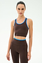 A person stands facing forward against a plain light background, wearing the SPLITS59 Amber Airweight Bralette in Dark Chocolate/Classic Blue, made from Airweight performance fabric—perfect for hot yoga.