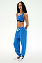 A woman stands against a plain light background wearing the SPLITS59 Andie Oversized Fleece Sweatpant in Classic Blue, paired with a matching sports bra and white sneakers—an ideal look for cool weather workouts.