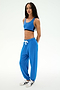 A woman stands against a plain light background wearing the SPLITS59 Andie Oversized Fleece Sweatpant in Classic Blue, paired with a matching sports bra and white sneakers—an ideal look for cool weather workouts.