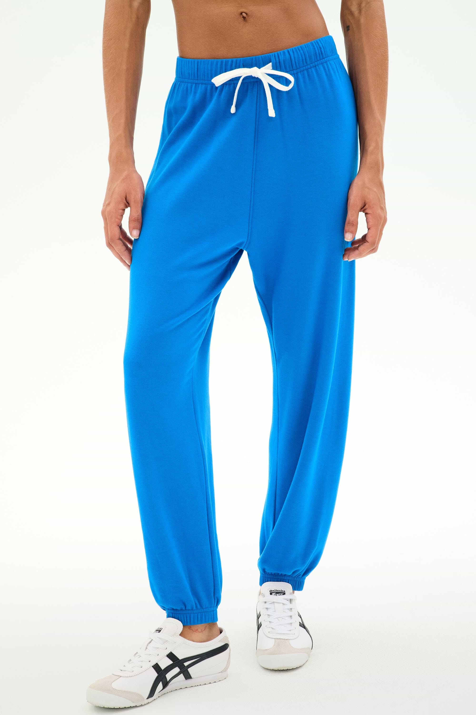 Model wearing SPLITS59 Andie Oversized Fleece Sweatpant in Classic Blue paired with white sneakers, standing against a plain white background—the ideal outfit for cool weather workouts.