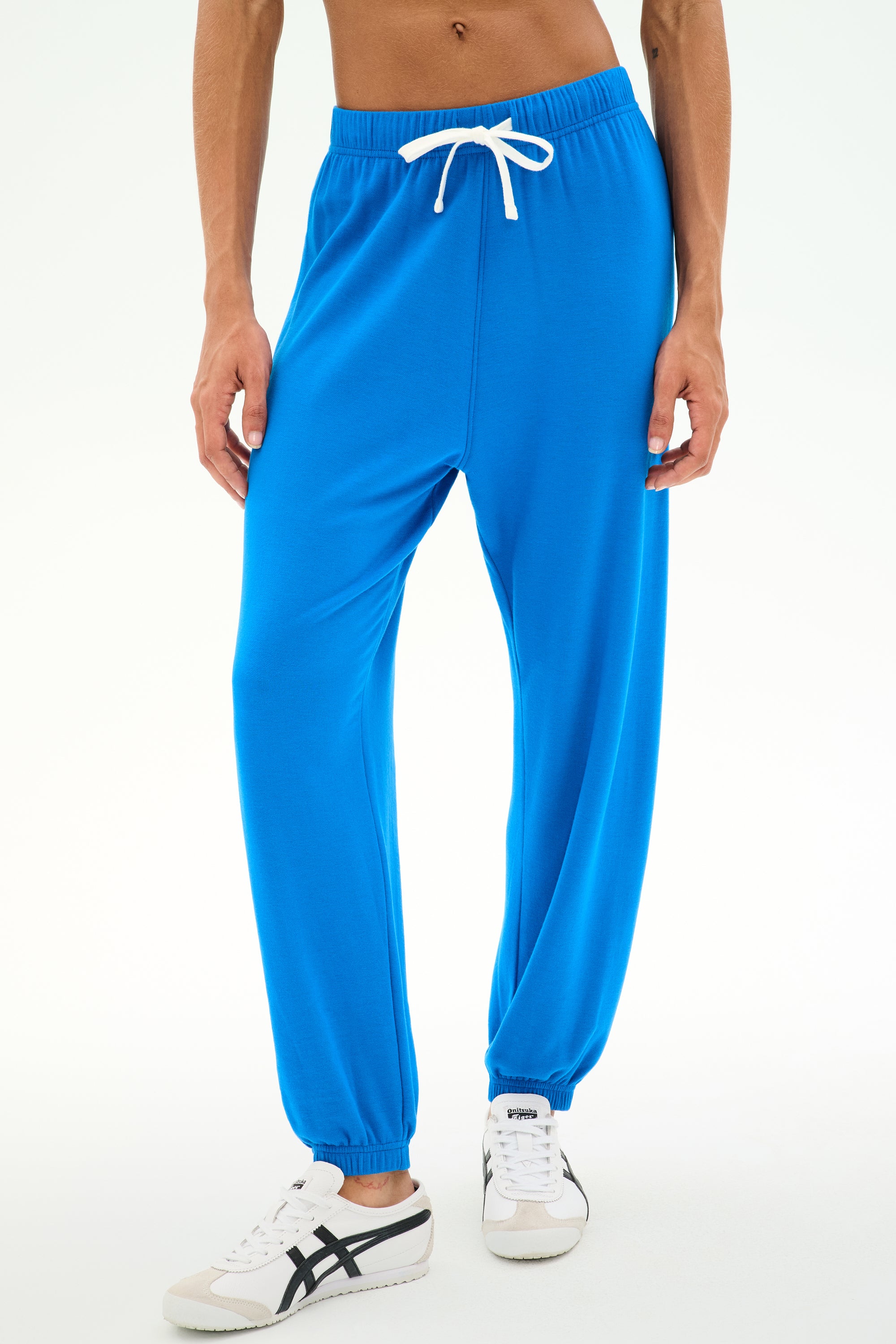 Model wearing SPLITS59 Andie Oversized Fleece Sweatpant in Classic Blue paired with white sneakers, standing against a plain white background—the ideal outfit for cool weather workouts.