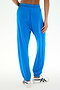 A person wearing the SPLITS59 Andie Oversized Fleece Sweatpant in Classic Blue and white sandals stands with one hand on their hip, shown from the back against a plain background. Made in Los Angeles, these baggy fleece sweatpants combine comfort and style—perfect for cool weather workouts.