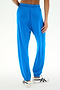 A person wearing the SPLITS59 Andie Oversized Fleece Sweatpant in Classic Blue and white sandals stands with one hand on their hip, shown from the back against a plain background. Made in Los Angeles, these baggy fleece sweatpants combine comfort and style—perfect for cool weather workouts.