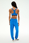 Facing away from the camera against a plain white background, a person wears SPLITS59's Andie Oversized Fleece Sweatpant in Classic Blue paired with a matching blue sports bra and white sneakers—an ideal cool weather workout look.