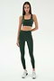 A woman stands against a plain background wearing the SPLITS59 Margot Rigor Legging in Military/Blush and a matching dark green sports bra, paired with white sneakers.