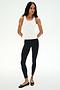 A woman poses against a white background in the SPLITS59 Mel Airweight Lite Tank - White, paired with black side-stripe leggings and black ballet flats—ideal for Pilates or hot yoga.