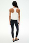 A person stands on a white background, facing away, wearing the SPLITS59 Mel Airweight Lite Tank in white—ideal for Pilates—paired with black leggings featuring white side stripes and black flats.