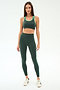 A woman stands against a plain background wearing the SPLITS59 Robbie Airweight Bra in Military/Spearmint with matching leggings, featuring green and white trim, paired with white sneakers.