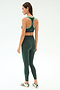 A woman stands in profile facing left, wearing SPLITS59 Robbie Airweight Bra in Military/Spearmint with matching leggings and white athletic shoes against a plain light background.