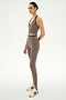A person stands in profile against a plain white background wearing the SPLITS59 River Dual Waist Airweight Stirrup Leggings in Lentil/Black, featuring a fitted silhouette crafted from stretch fabric, paired with a matching taupe athletic crop top and white athletic shoes.