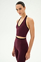 A woman wearing the SPLITS59 Rory Airweight Halter Bralette in Dark Cherry/Black, paired with matching high-waisted leggings, both crafted from a stretchy nylon-spandex blend, stands against a plain white background.