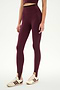 A person wearing the SPLITS59 River Dual Waist Airweight Stirrup leggings in Dark Cherry/Black, featuring a high-waisted fit and stirrup design crafted from smooth nylon spandex fabric, styled with a matching crop top and cream sneakers with maroon stripes, stands against a plain white background.