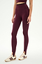 A person wearing the SPLITS59 River Dual Waist Airweight Stirrup leggings in Dark Cherry/Black, featuring a high-waisted fit and stirrup design crafted from smooth nylon spandex fabric, styled with a matching crop top and cream sneakers with maroon stripes, stands against a plain white background.
