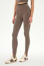 Wearing SPLITS59′s River Dual Waist Airweight Stirrup leggings in Lentil/Black, this individual stands against a plain white background.