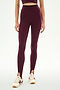 A person wears the SPLITS59 River Dual Waist Airweight Stirrup leggings in Dark Cherry/Black, paired with a matching crop top and white sneakers featuring burgundy stripes, standing against a plain background.