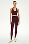 A person stands against a white background wearing the SPLITS59 Rory Airweight Halter Bralette in Dark Cherry/Black, paired with matching high-waisted leggings made from stretchy nylon spandex fabric and cream-colored sneakers.
