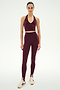 A person stands against a white background wearing the SPLITS59 Rory Airweight Halter Bralette in Dark Cherry/Black, paired with matching high-waisted leggings made from stretchy nylon spandex fabric and cream-colored sneakers.