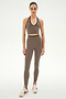 A woman stands facing forward, wearing the SPLITS59 Rory Airweight Halter Bralette in Lentil/Black paired with matching high-waisted leggings featuring stirrups. Both pieces are crafted from athletic stretch fabric for a supportive fit. She completes the look with beige sneakers, set against a plain white background.