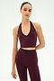 A woman wearing the SPLITS59 Rory Airweight Halter Bralette in Dark Cherry/Black, paired with matching high-waisted leggings, both crafted from stretchy nylon spandex fabric, stands against a plain white background.