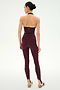 A person stands with their back to the camera, wearing the SPLITS59 River Dual Waist Airweight Stirrup leggings in Dark Cherry/Black, with their hair in a bun and beige athletic shoes.
