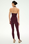 A person stands with their back to the camera, wearing the SPLITS59 River Dual Waist Airweight Stirrup leggings in Dark Cherry/Black, with their hair in a bun and beige athletic shoes.