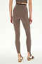 A person stands facing away, styled in SPLITS59’s River Dual Waist Airweight Stirrup leggings in Lentil/Black—a high-waisted design with stirrups crafted from a stretchy nylon-spandex blend—paired with a matching crop top and white sneakers featuring maroon and tan accents, set against a plain background for an effortlessly contemporary athletic look.