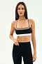 A woman stands against a plain background wearing the SPLITS59 Scottie Airweight Bra in Black/Lentil with white trim and matching high-waisted leggings, both crafted from soft nylon and spandex for a comfortable, flexible fit.